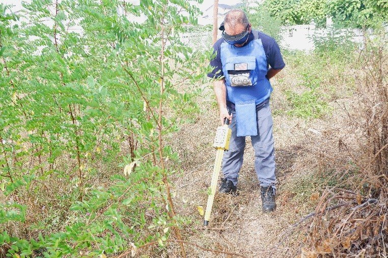 Halo Trust deminer with a Schonstedt magnetic locator in vegetation